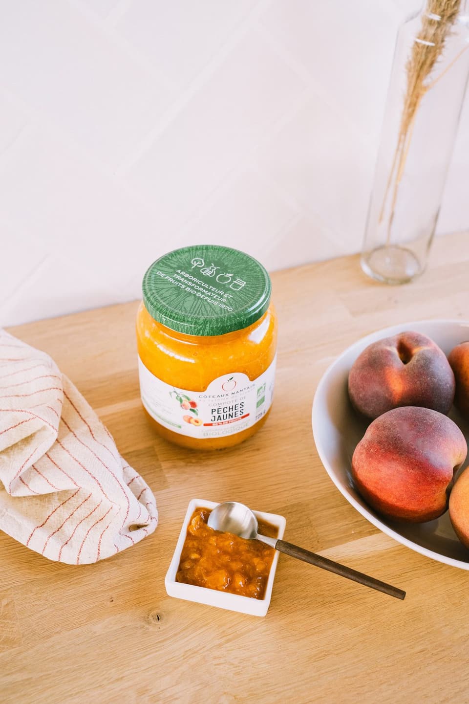 Jar of yellow peach compote on a wooden table, next to peaches